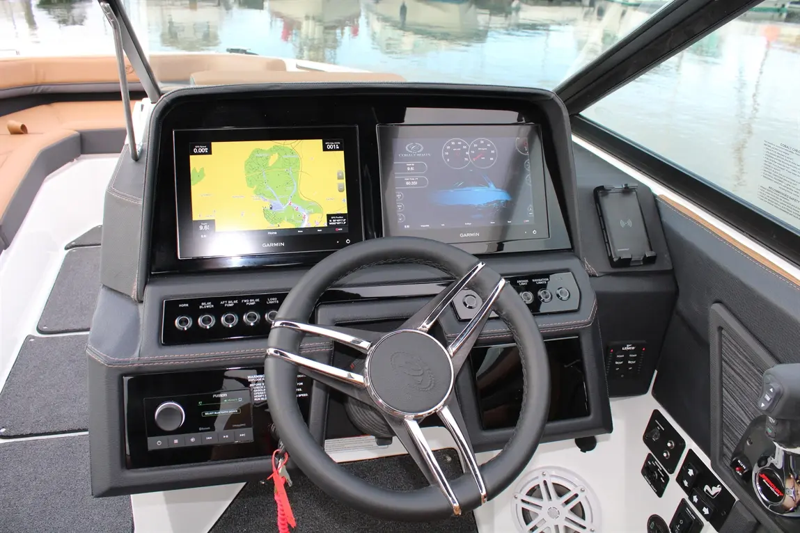 Modern boat cockpit featuring Garmin displays, steering wheel, and controls with a waterfront view in the background.